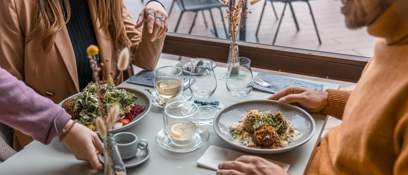 Zwei Personen sitzen an einem Tisch im Killesberg Restaurant Bellevue, genießen Salat und Pasta. Der Tisch ist elegant gedeckt mit Getränken und Dekoration., © Stuttgart-Marketing GmbH, Martina Denker