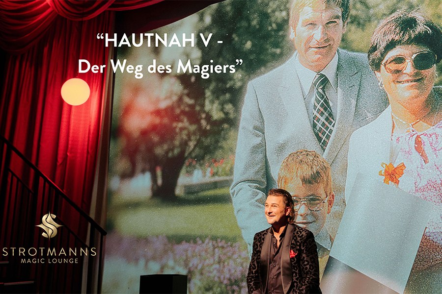 Ein Magier steht vor einem großen Familienfoto, Titel 'HAUTNAH V - Der Weg des Magiers'. Bühne mit rotem Vorhang, Logo von Strotmanns Magic Lounge., © Strotmanns Magic Lounge Ein Magier steht vor einem großen Familienfoto, Titel 'HAUTNAH V - Der Weg des Magiers'. Bühne mit rotem Vorhang, Logo von Strotmanns Magic Lounge., © Strotmanns Magic Lounge