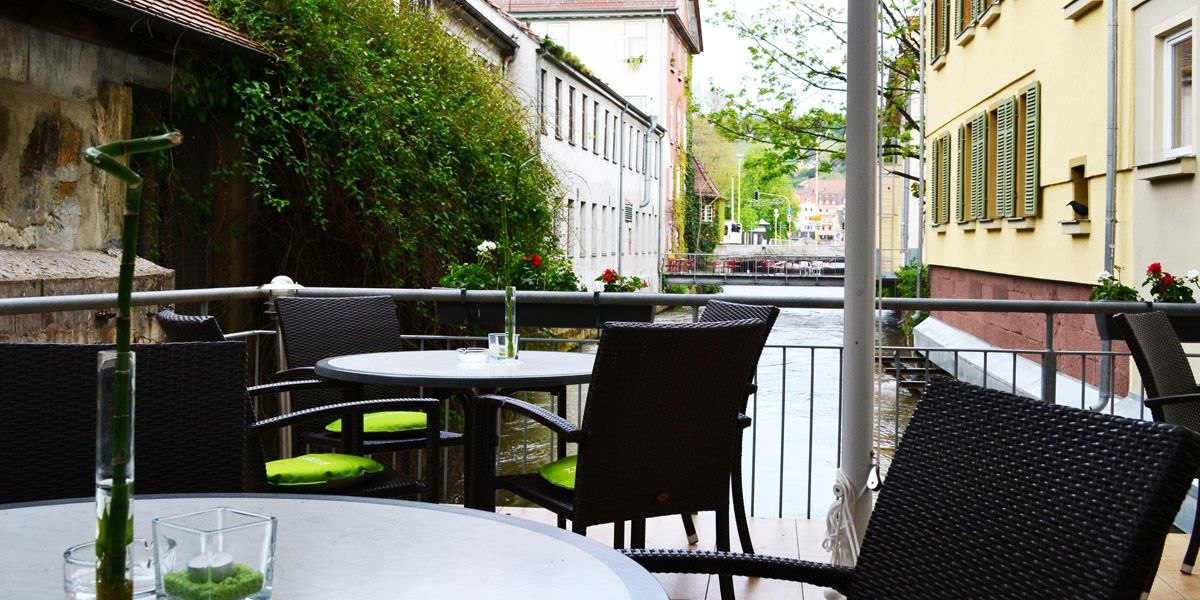 Cozy terrace with round tables and chairs, view of a river between two buildings, decorated with plants., &copy; ECOINN Hotel am Campus