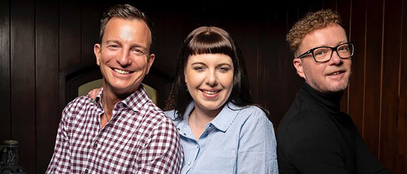 Three people stand smiling next to each other in front of a wooden wall. They are wearing casual clothes and appear cheerful., © Zumbecher Three people stand smiling next to each other in front of a wooden wall. They are wearing casual clothes and appear cheerful., © Zumbecher