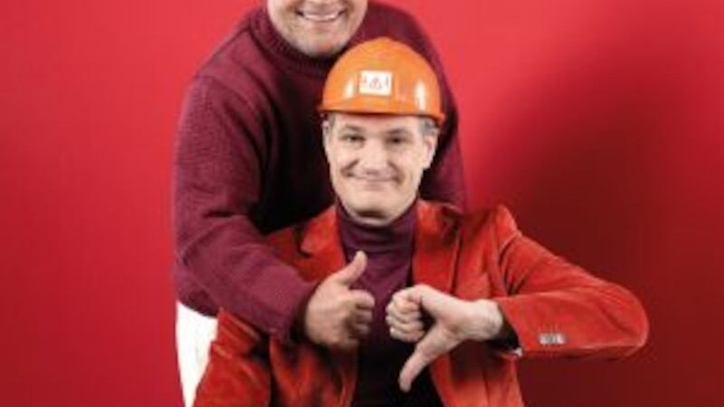 Two men in front of a red background. One is wearing a construction helmet and giving a thumbs-up, the other a thumbs-down. Both are smiling., &copy; Altes Schauspielhaus und Kom&ouml;die im Marquardt e.V.