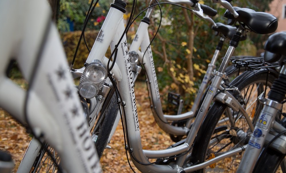 White bicycles are lined up on the ground, which is covered with autumn leaves. The frames are adorned with lettering., &copy; Hotel B&uuml;rkle