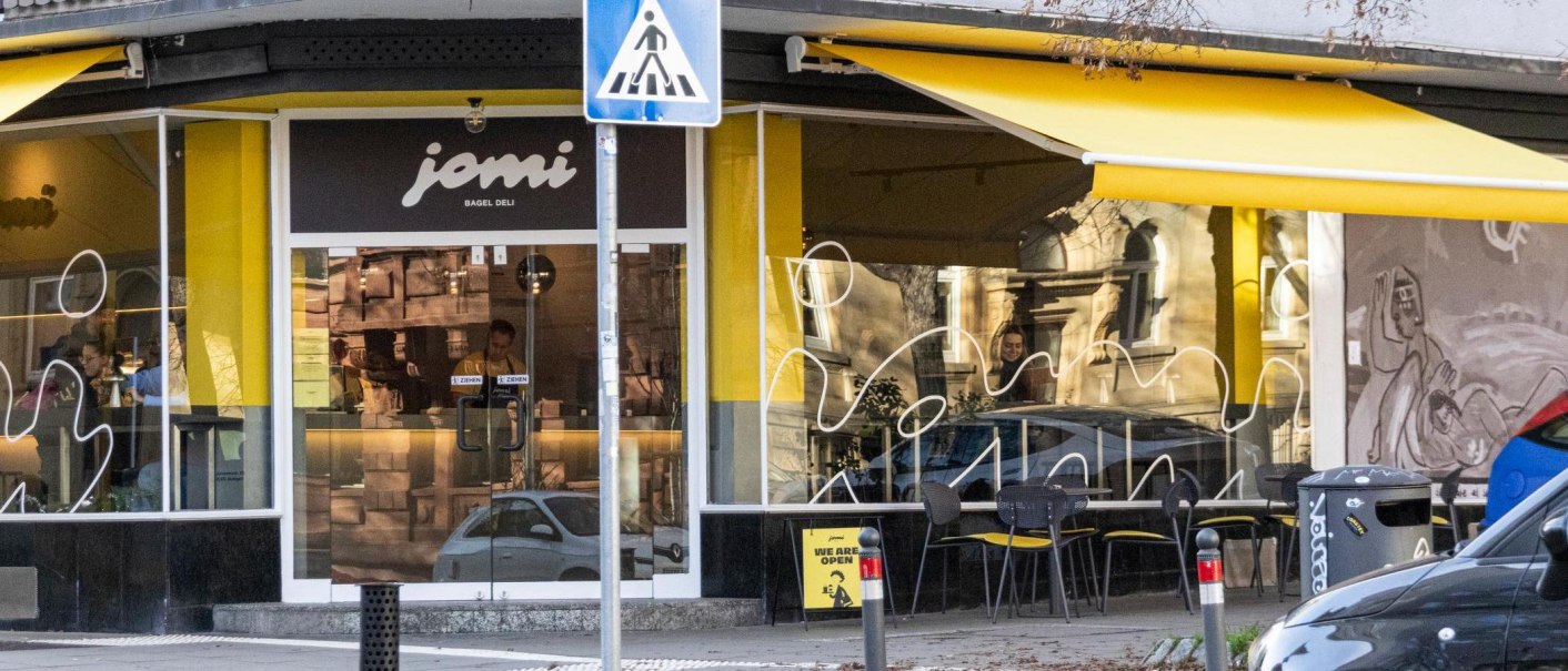 Shop window of the deli with yellow awnings. Above the door at the corner of the building it says "jomi Bagel Deli"., &copy; Stuttgart-Marketing GmbH, Sarah Schmid