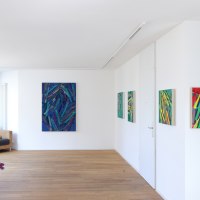 Gallery with abstract paintings on white walls, wooden floor, armchair and purple flowers in a vase., &copy; Galerie Klaus Braun