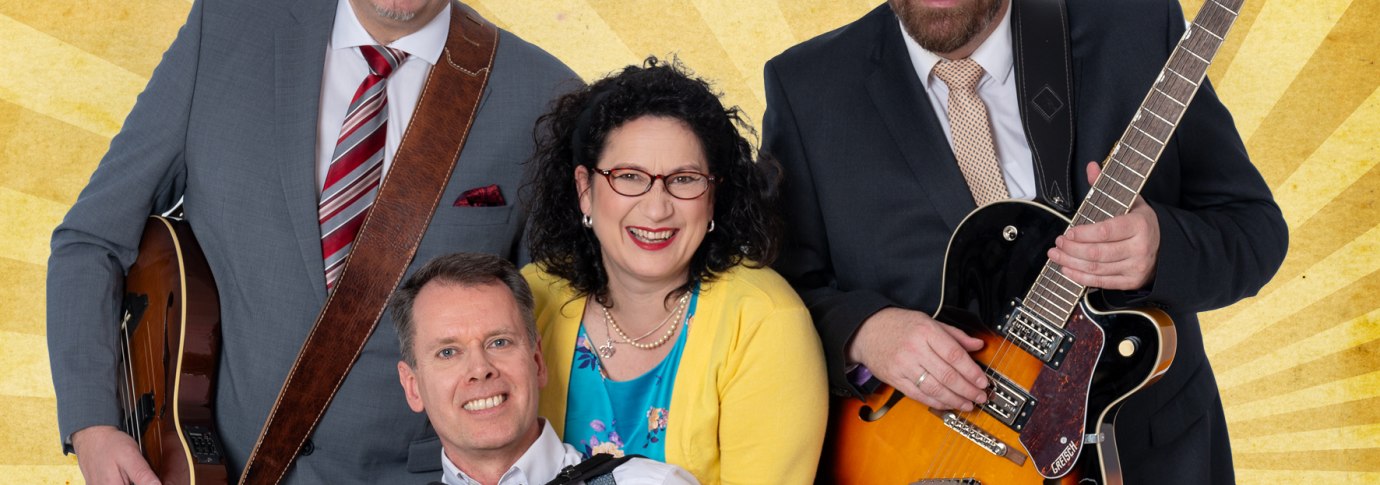 Vier Personen posieren fr&ouml;hlich mit Instrumenten vor einem gelben Strahlenhintergrund. Zwei M&auml;nner halten Gitarren, einer ein Akkordeon, eine Frau steht in der Mitte., &copy; Friedrichsdbau Variet&eacute;