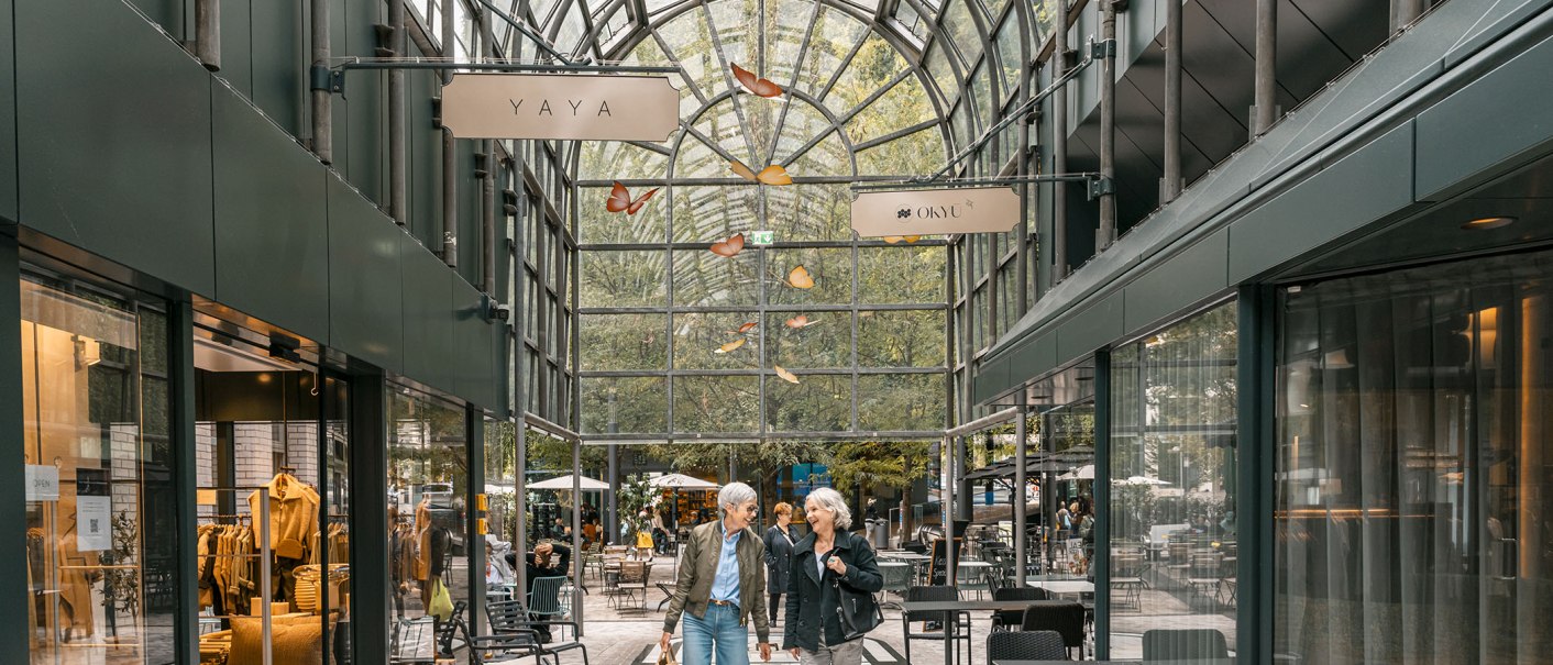 Zwei Personen schlendern durch die Calwer Passage mit Geschäften und Cafés unter einem gewölbten Glasdach., © Stuttgart-Marketing GmbH, Sarah Schmid Zwei Personen schlendern durch die Calwer Passage mit Geschäften und Cafés unter einem gewölbten Glasdach., © Stuttgart-Marketing GmbH, Sarah Schmid