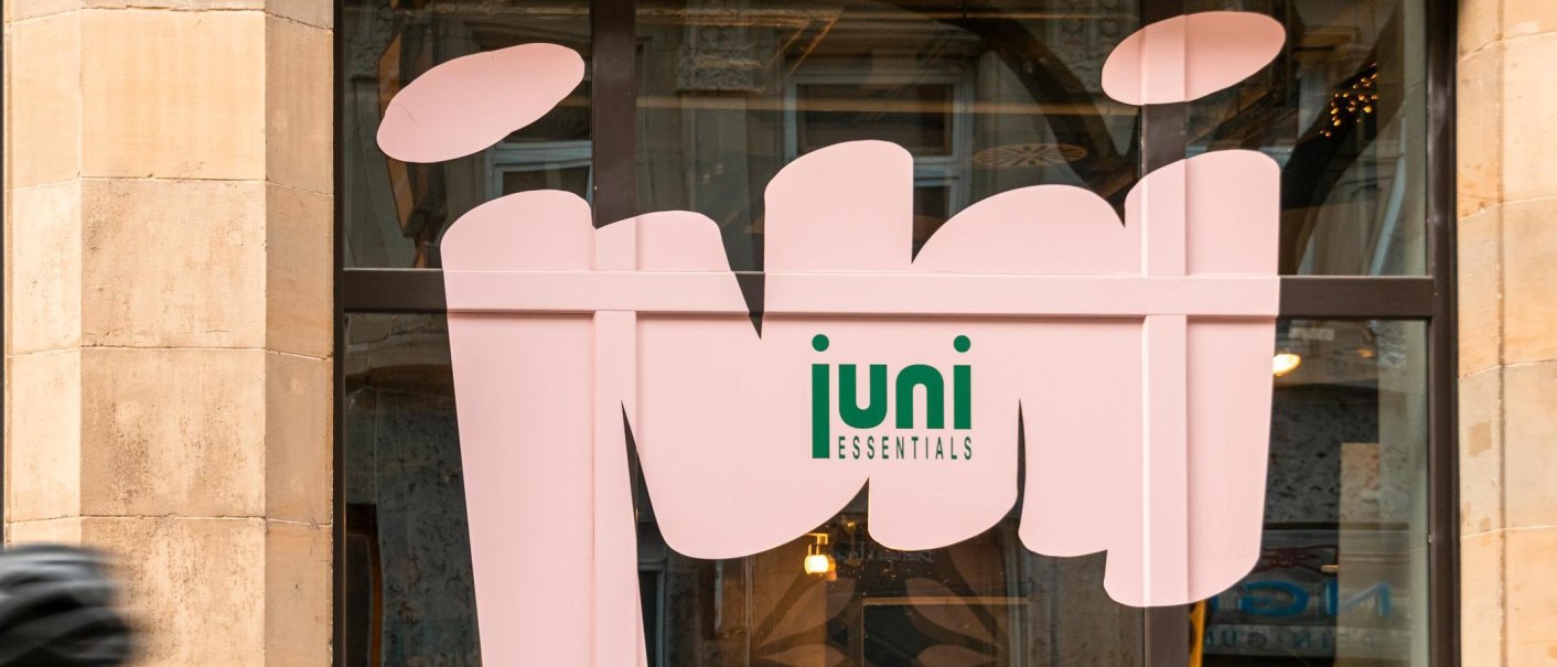 Ein Schaufenster mit einem großen rosa Schriftzug 'juni ESSENTIALS' auf Glas. Im Hintergrund sind unscharfe Innenräume zu sehen., © SMG, Sarah Schmid Ein Schaufenster mit einem großen rosa Schriftzug 'juni ESSENTIALS' auf Glas. Im Hintergrund sind unscharfe Innenräume zu sehen., © SMG, Sarah Schmid