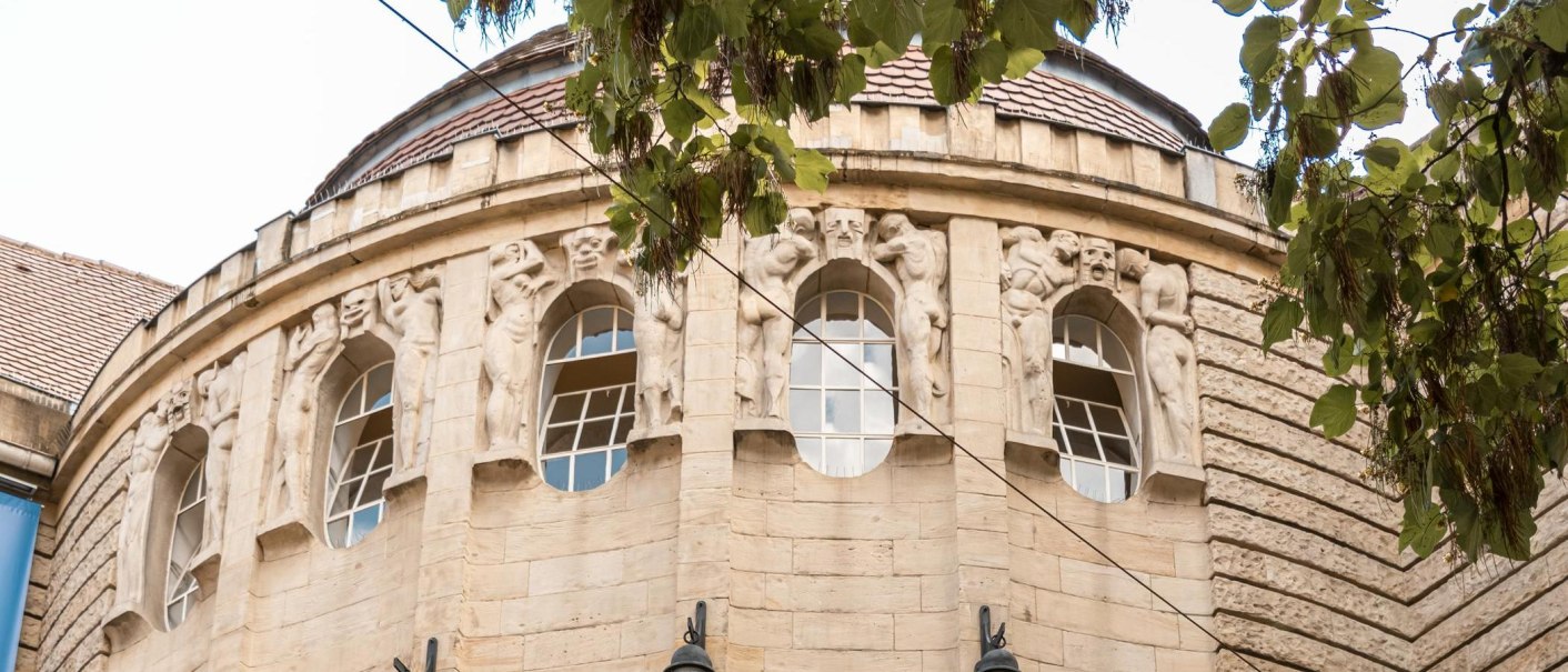 Fassade des Alten Schauspielhauses mit kunstvollen Skulpturen zwischen den Fenstern, umgeben von grünen Blättern eines Baumes., © Stuttgart-Marketing GmbH, Sarah Schmid Fassade des Alten Schauspielhauses mit kunstvollen Skulpturen zwischen den Fenstern, umgeben von grünen Blättern eines Baumes., © Stuttgart-Marketing GmbH, Sarah Schmid