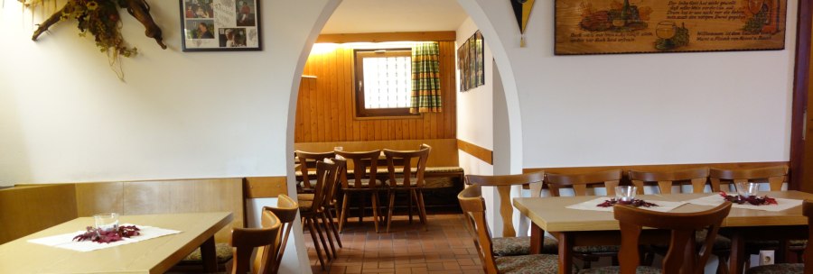 A cozy restaurant with wooden tables and chairs, decorated with pictures and flowers. An arch leads into another room., © Besenwirtschaft Familie Nerz A cozy restaurant with wooden tables and chairs, decorated with pictures and flowers. An arch leads into another room., © Besenwirtschaft Familie Nerz