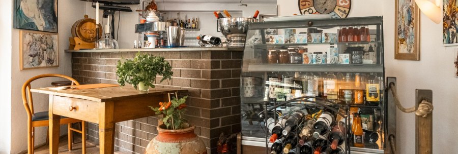 Gem&uuml;tliches Caf&eacute; mit Holztisch, Weinregal, dekorativen Bildern und Pflanzen. Eine Theke mit Getr&auml;nken und ein Fernseher sind ebenfalls zu sehen., &copy; SMG, Sarah Schmid