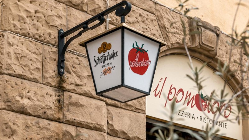 Ein Schild mit Schöfferhofer-Logo und Tomatenmotiv hängt an einer Steinwand vor dem Restaurant 'il pomodoro'., © SMG, Sarah Schmid Ein Schild mit Schöfferhofer-Logo und Tomatenmotiv hängt an einer Steinwand vor dem Restaurant 'il pomodoro'., © SMG, Sarah Schmid