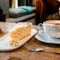 Ein Stück Kuchen und eine Tasse Kaffee auf einem Holztisch in einem gemütlichen Café. Im Hintergrund unscharfe Möbel., © Stuttgart-Marketing GmbH, Sarah Schmid
