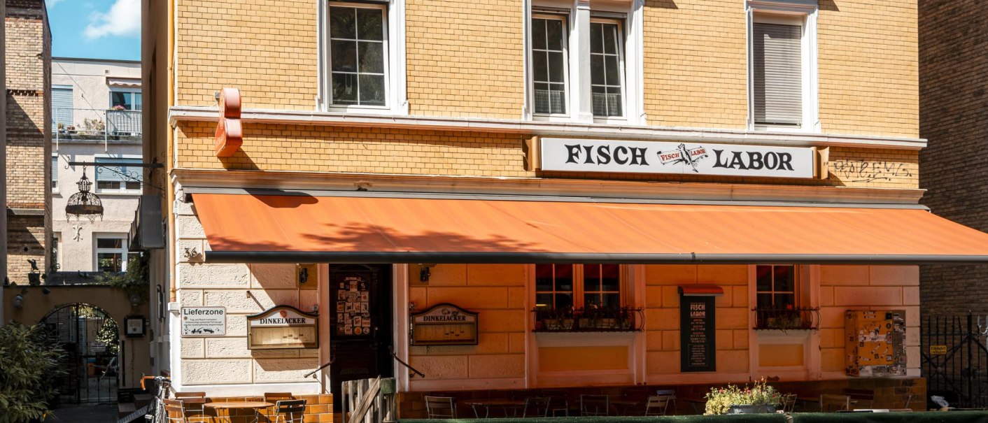 Ein Restaurant namens Fischlabor mit orangener Markise und Sitzgelegenheiten im Freien. Das Geb&auml;ude hat gelbe Ziegelw&auml;nde und wei&szlig;e Fensterrahmen., &copy; SMG, Sarah Schmid