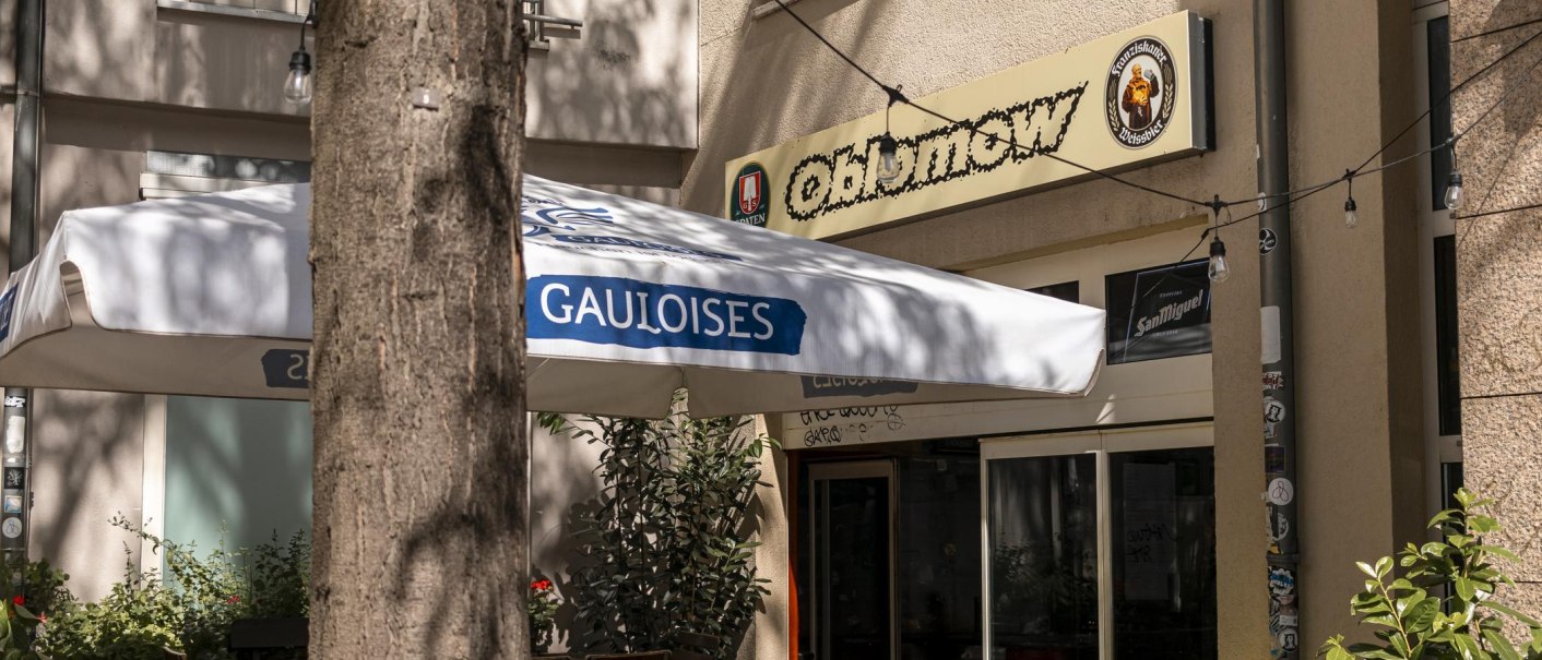 Entrance of a café called Oblamow with Gauloises parasol and plants. Exterior lighting and Franciscan and San Miguel signs visible., © SMG, Sarah Schmid