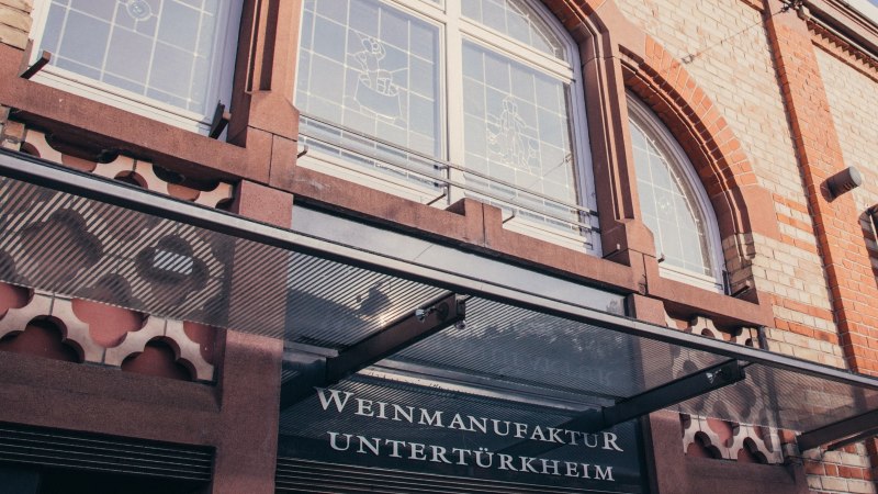 Fassade der Weinmanufaktur Untert&uuml;rkheim mit Glasvordach, Schriftzug und dekorativen Fenstern., &copy; Weinmanufaktur Stuttgart