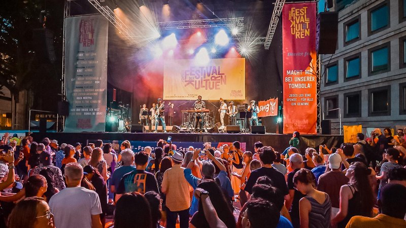 Große Menschenmenge vor einer Bühne beim Sommerfestival der Kulturen. Musiker spielen, bunte Lichter und Banner im Hintergrund., © Forum der Kulturen Stuttgart e. V.