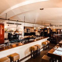 Ein stilvolles Restaurant mit Bar, Holzmöbeln und moderner Beleuchtung. Die Bar ist gut bestückt, und es gibt Sitzgelegenheiten mit gedeckten Tischen., © Amadeus Ein stilvolles Restaurant mit Bar, Holzmöbeln und moderner Beleuchtung. Die Bar ist gut bestückt, und es gibt Sitzgelegenheiten mit gedeckten Tischen., © Amadeus