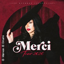 Frau mit schwarzem Hut und rotem Lippenstift vor rotem Vorhang. Text: Merci Tour 2026., © links im Bild