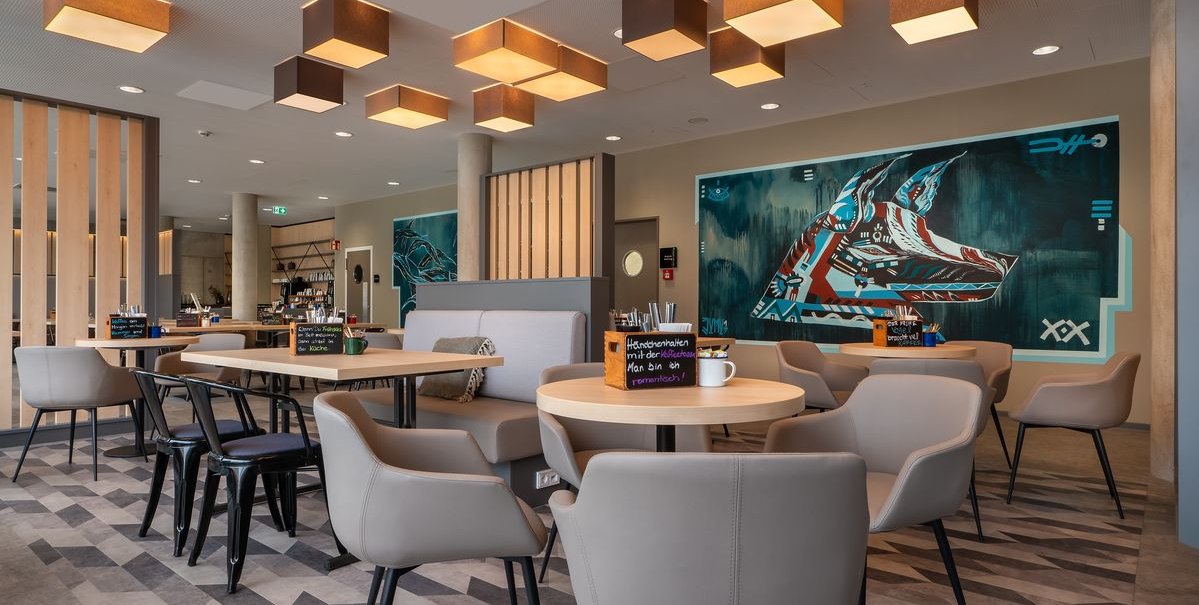 Modernes Restaurant mit stilvollen M&ouml;beln, geometrischen Deckenleuchten und Wandkunst. Runde Tische und bequeme St&uuml;hle schaffen eine einladende Atmosph&auml;re., &copy; Novum Hospitality