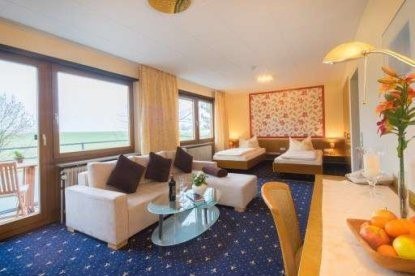 Bright hotel room with two beds, sofa, glass table and balcony. Floral pattern on the wall, fruit bowl and lamp on the table., © Kemnater Hof