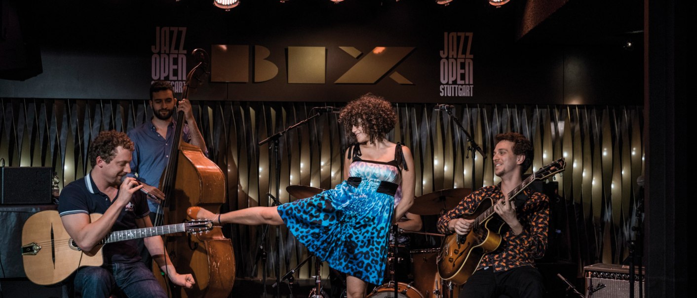 A band plays in the BIX jazz club. A guitarist, a double bass player and a singer in a blue dress can be seen. "Jazz Open Stuttgart" in the background., &copy; Peter Steinheisser