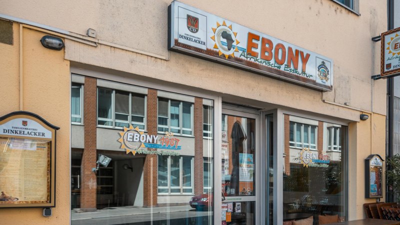 Entrance to the restaurant 'Ebony' with signs for African cuisine. Windows reflect the street opposite. Open since 1987., © SMG Stuttgart Marketing GmbH - Sarah Schmid Entrance to the restaurant 'Ebony' with signs for African cuisine. Windows reflect the street opposite. Open since 1987., © SMG Stuttgart Marketing GmbH - Sarah Schmid