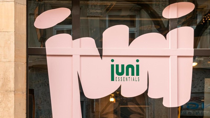 Ein Schaufenster mit einem gro&szlig;en rosa Schriftzug 'juni ESSENTIALS' auf Glas. Im Hintergrund sind unscharfe Innenr&auml;ume zu sehen., &copy; SMG, Sarah Schmid