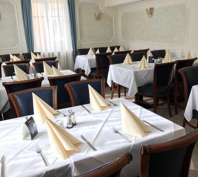 Elegantes Restaurant mit weiß gedeckten Tischen, gefalteten Servietten und blauen Vorhängen. Klassische Holzmöbel und Kronleuchter sorgen für ein stilvolles Ambiente., © Hotel Engelhof