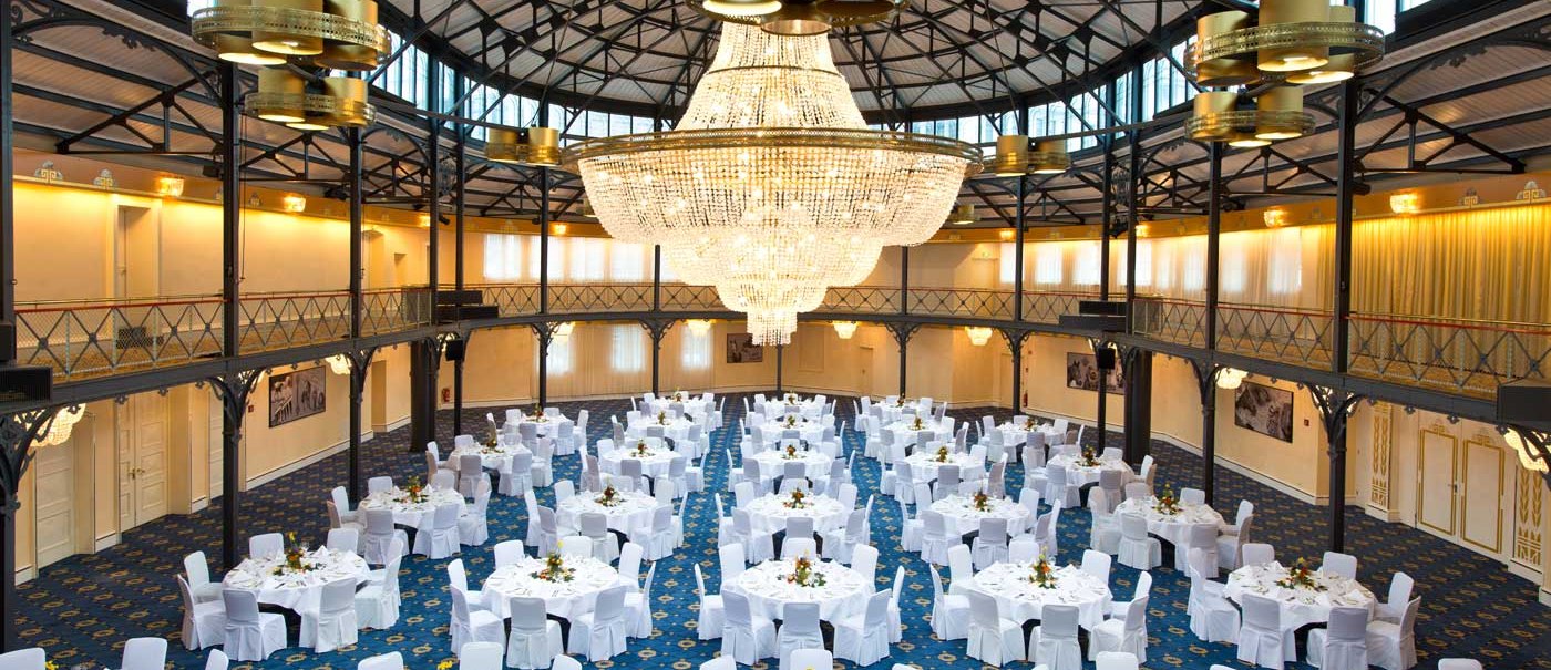 Die Alte Stuttgarter Reithalle mit elegant gedeckten Tischen und einem beeindruckenden Kronleuchter unter einem hohen, gewölbten Dach., © Maritim Hotelgesellschaft mbH Die Alte Stuttgarter Reithalle mit elegant gedeckten Tischen und einem beeindruckenden Kronleuchter unter einem hohen, gewölbten Dach., © Maritim Hotelgesellschaft mbH