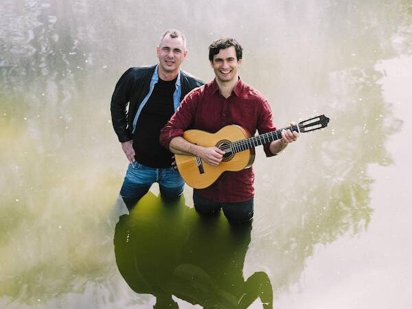 Zwei Männer stehen bis zu den Knien in einem Teich. Einer trägt eine Gitarre und lächelt. Ihre Spiegelbilder sind im Wasser sichtbar., © Rosenau Kultur e.V. Zwei Männer stehen bis zu den Knien in einem Teich. Einer trägt eine Gitarre und lächelt. Ihre Spiegelbilder sind im Wasser sichtbar., © Rosenau Kultur e.V.