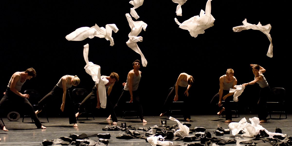 Tänzer auf einer dunklen Bühne werfen weiße Tücher in die Luft. Sie tragen schwarze Kleidung und bewegen sich synchron., © Regina Brocke