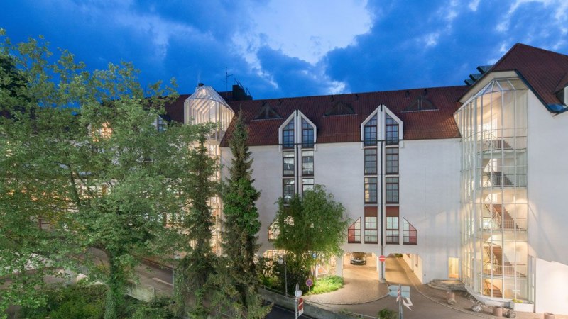 The Best Western Plus Hotel am Schlossberg at dusk, with illuminated windows and a glass staircase surrounded by trees., © Best Western Plus Hotel am Schlossberg The Best Western Plus Hotel am Schlossberg at dusk, with illuminated windows and a glass staircase surrounded by trees., © Best Western Plus Hotel am Schlossberg
