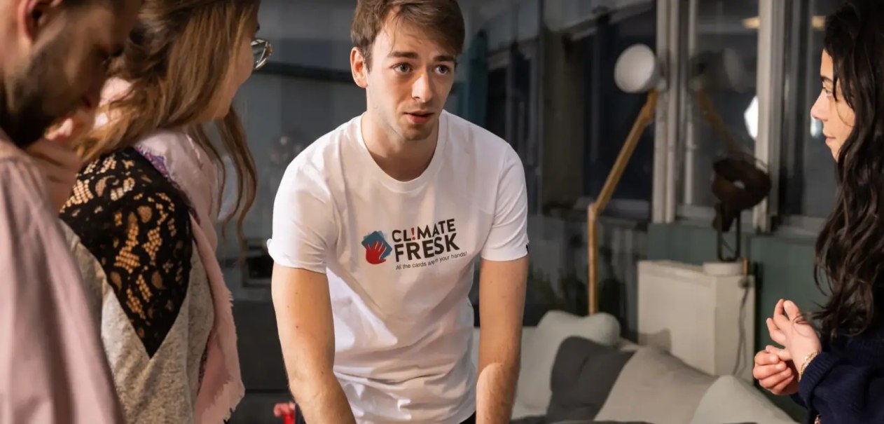 Ein Mann im Climate Fresk T-Shirt erklärt etwas in einem Workshop. Zwei Frauen hören aufmerksam zu. Der Raum ist modern eingerichtet., © Climate Fresk Deutschland e. V. Ein Mann im Climate Fresk T-Shirt erklärt etwas in einem Workshop. Zwei Frauen hören aufmerksam zu. Der Raum ist modern eingerichtet., © Climate Fresk Deutschland e. V.