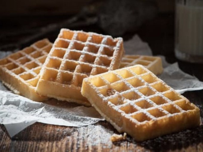 Vier goldbraune Waffeln mit Puderzucker bestreut, auf Backpapier präsentiert. Im Hintergrund ein Glas Milch., © Cool-Tours StattReisen Vier goldbraune Waffeln mit Puderzucker bestreut, auf Backpapier präsentiert. Im Hintergrund ein Glas Milch., © Cool-Tours StattReisen