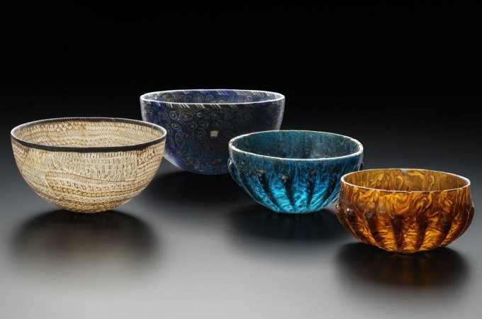 Vier kunstvoll gestaltete Glasschalen in verschiedenen Farben und Mustern, die auf einem schwarzen Hintergrund pr&auml;sentiert werden., &copy; Landesmuseum W&uuml;rttemberg