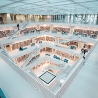 Moderne, helle Bibliothek mit mehreren Etagen, weißen Wänden und Bücherregalen. Menschen bewegen sich auf den Treppen und lesen Bücher., © Stuttgart-Marketing GmbH, Sarah Schmid