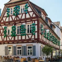 Half-timbered house in Kirchheim unter Teck with green shutters. In front of the building are tables and chairs from a street café., © Stuttgart-Marketing GmbH, Sarah Schmid