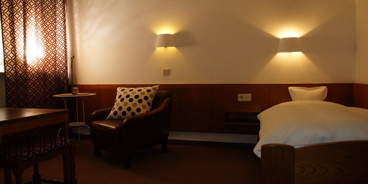 Ein gemütliches Einzelzimmer mit einem Bett, einem braunen Ledersessel mit gepunktetem Kissen, einem kleinen Tisch und gemusterten Vorhängen., © Hotelmärchen Ein gemütliches Einzelzimmer mit einem Bett, einem braunen Ledersessel mit gepunktetem Kissen, einem kleinen Tisch und gemusterten Vorhängen., © Hotelmärchen