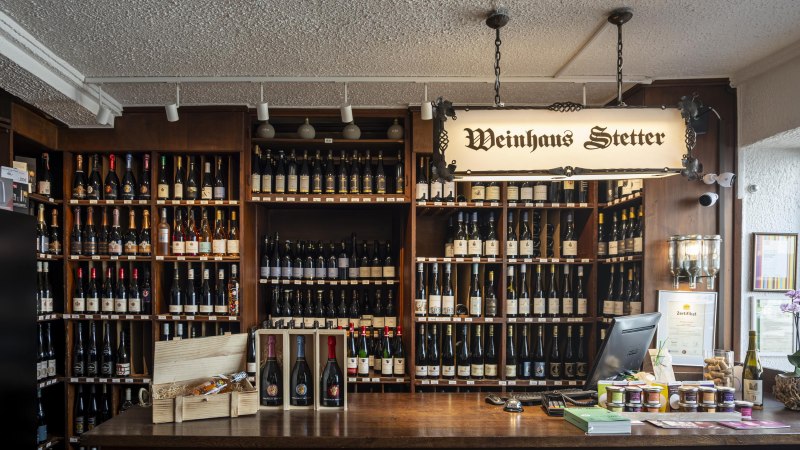 Theke im Weinhaus Stetter mit Regalen voller Weinflaschen und einem hölzernen Tresen. Ein Schild mit der Aufschrift 'Weinhaus Stetter' hängt von der Decke., © Stuttgart Marketing GmbH, Sarah Schmid