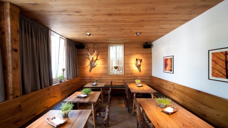A cozy restaurant with wooden tables, plants on the tables, and decorative elements on the walls. The wooden walls and ceiling create a warm atmosphere., © Ruthenberg&Schlatter GbR A cozy restaurant with wooden tables, plants on the tables, and decorative elements on the walls. The wooden walls and ceiling create a warm atmosphere., © Ruthenberg&Schlatter GbR