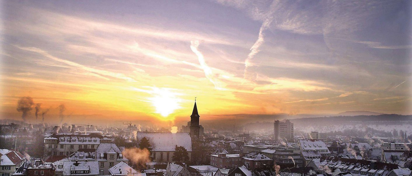 Göppingen in winter: Snow-covered roofs and church tower at sunrise, with smoking chimneys and a cloudy sky., © Stuttgart-Marketing GmbH Göppingen in winter: Snow-covered roofs and church tower at sunrise, with smoking chimneys and a cloudy sky., © Stuttgart-Marketing GmbH