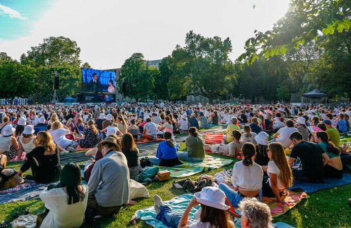 Viele Menschen sitzen auf Decken im Park und schauen auf eine große Leinwand. Die Atmosphäre ist entspannt und sommerlich., © Württembergische Staatstheater Stuttgart Viele Menschen sitzen auf Decken im Park und schauen auf eine große Leinwand. Die Atmosphäre ist entspannt und sommerlich., © Württembergische Staatstheater Stuttgart