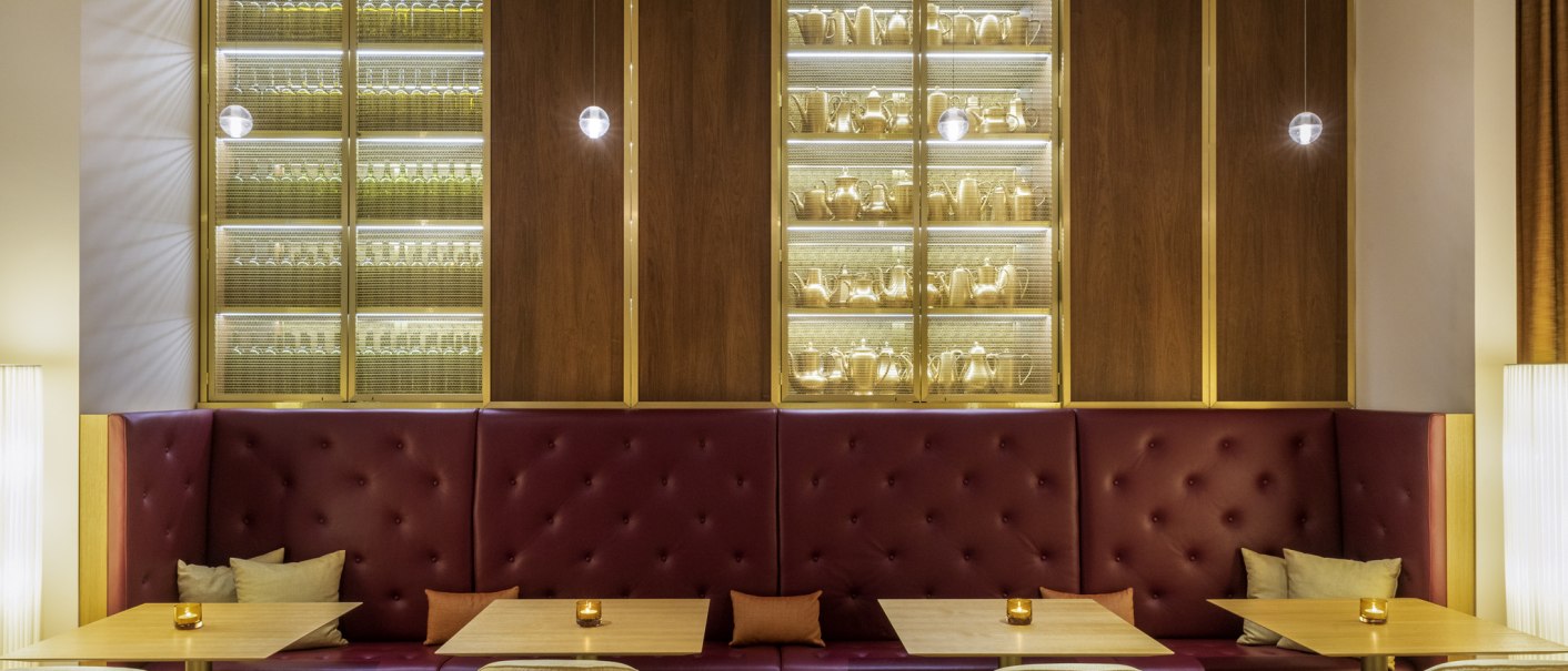 Elegante Bar mit roten Sitzbänken, Holztischen und beleuchteten Regalen voller Gläser und Karaffen. Dezente Beleuchtung schafft eine gemütliche Atmosphäre., © Mövenpick Hotel Stuttgart Messe & Congress