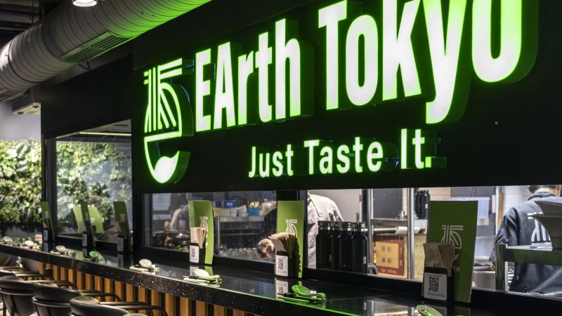 Restaurant with green illuminated sign 'EArth Tokyo' and the slogan 'Just Taste It'. Modern interior with plant wall., © SMG, Sarah Schmid