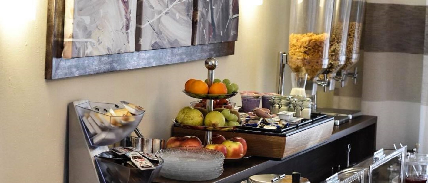 A rich breakfast buffet with bread rolls, cold cuts, fruit, muesli and drinks. An abstract painting on the wall in the background., &copy; TOMAS