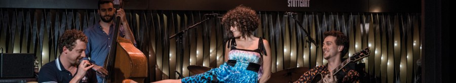 Eine Band spielt im BIX Jazzclub. Ein Gitarrist, ein Kontrabassist und eine Sängerin in blauem Kleid sind zu sehen. "Jazz Open Stuttgart" im Hintergrund., © Peter Steinheisser