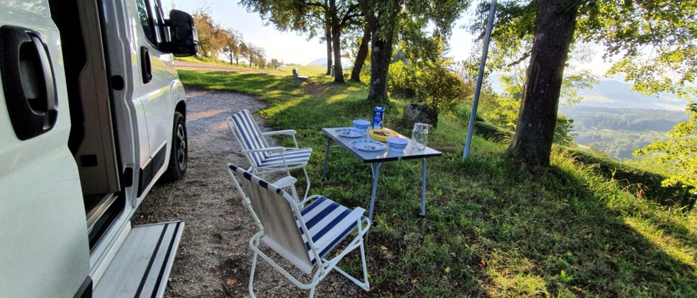 Wohnmobilstellplatz mit Tisch und St&uuml;hlen im Gr&uuml;nen. Teller und Gl&auml;ser auf dem Tisch, umgeben von B&auml;umen und mit Blick auf die Landschaft., &copy; Stadtmarketing G&ouml;ppingen