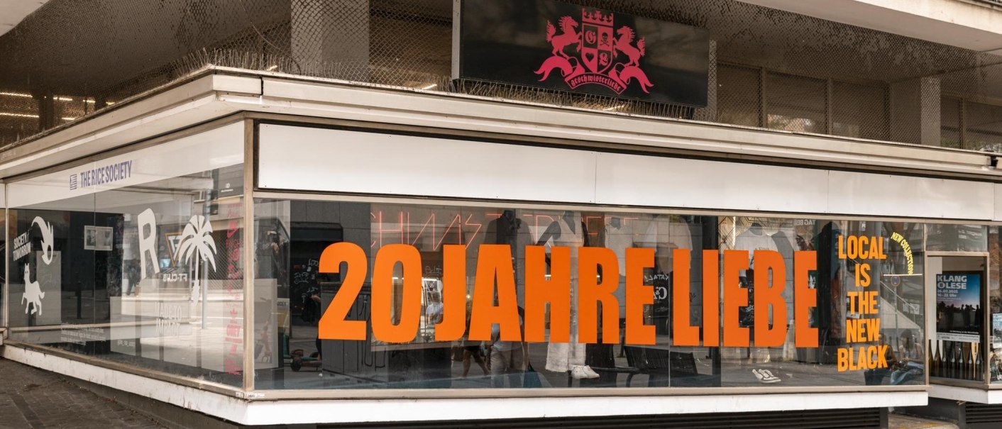 Store front with large display window, lettering '20 years of love' in orange. Above a sign with coat of arms and 'Geschwisterliebe'. Inside decoration and poster., © Stuttgart-Marketing GmbH, Sarah Schmid Store front with large display window, lettering '20 years of love' in orange. Above a sign with coat of arms and 'Geschwisterliebe'. Inside decoration and poster., © Stuttgart-Marketing GmbH, Sarah Schmid