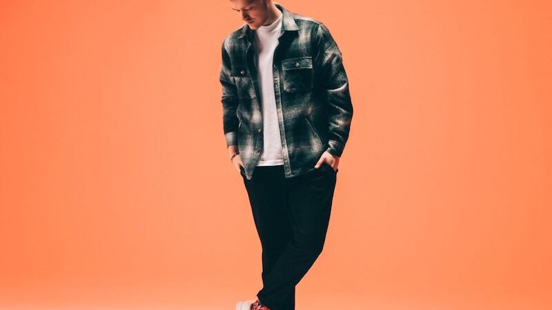 Eine Person in l&auml;ssiger Kleidung steht vor einem orangefarbenen Hintergrund und schaut nach unten., &copy; Theaterhaus Stuttgart e.V.