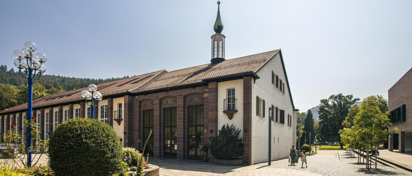 A historic building in Bad Liebenzell with a striking tower, surrounded by green countryside. People are strolling along the paved path., © SMG Stuttgart Marketing GmbH - Sarah Schmid A historic building in Bad Liebenzell with a striking tower, surrounded by green countryside. People are strolling along the paved path., © SMG Stuttgart Marketing GmbH - Sarah Schmid